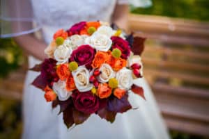 Bride holding fall wedding bouquet with white, red, and orange roses