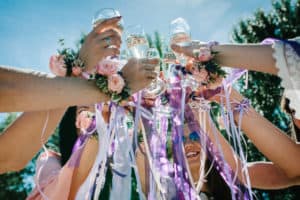 The hands of girls with boutonnieres and ribbons hold and raise glasses of champagne up. champagne glass decorated with flowers. Party in Style boho. Maiden evening Hen-parties. Bachelorette. Close up