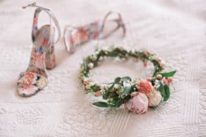 Wedding bride's wreath of white, pink flowers, orange berries and greens lying on a bed next to the bride's shoes