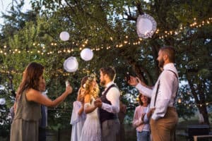 Guests with smartphones taking photo of bride and groom at wedding reception outside.