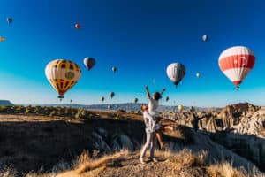 Wedding travel. Honeymoon trip. Couple in love among balloons. A guy proposes to a girl. Couple in love in Cappadocia. Couple in Turkey. Man and woman traveling. Festival of balloons. Tourists