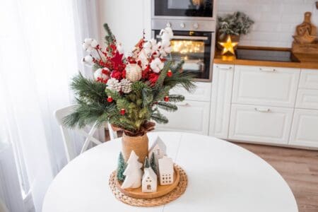 A spruce bouquet with red berries, toys, cotton on a white kitchen table. Christmas decorations in the interior. The concept of preparation for the New Year's holiday 2024.